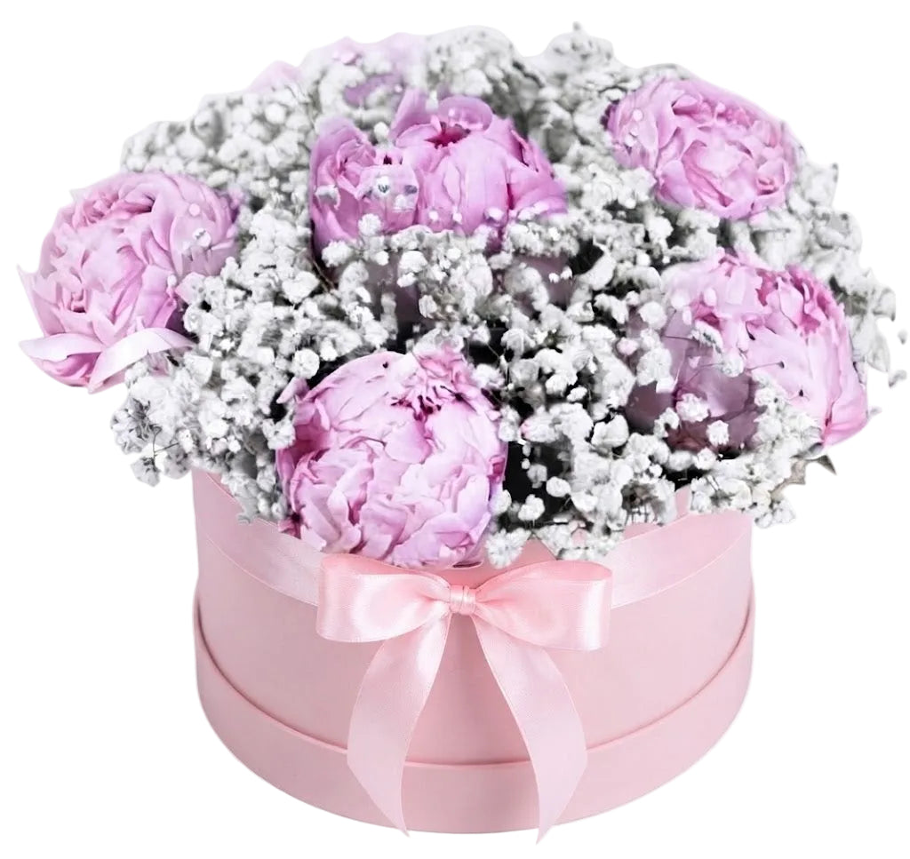 A round pink gift box filled with a bouquet of light purple peonies and white baby's breath, tied with a pink satin bow, on a white background.
